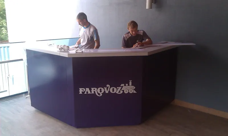 Угловая барная стойка с логотипом PAROVOZ на тёмном фасаде и светлой столешницей