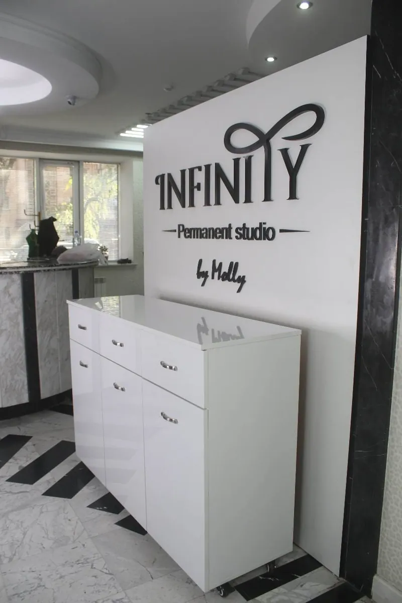 Белый комод и щит с логотипом INFINITY в холле студии