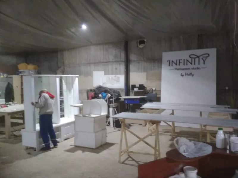 На производстве: белая мебель для студии и щит с логотипом INFINITY, мастер за работой