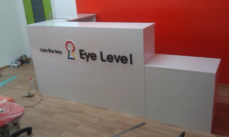 Белая стойка в два уровня с объёмным логотипом Eye Level на красной стене