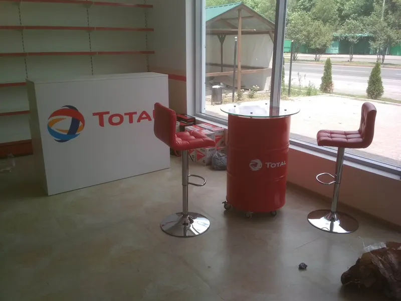Стойка с логотипом TOTAL, рядом стол из бочки и барные стулья