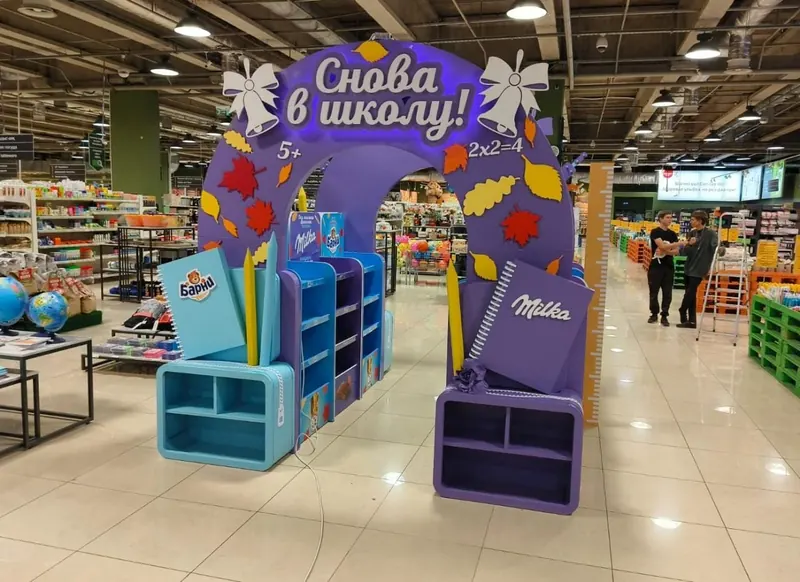 Зона бренда в торговом зале супермаркета: арка «Снова в школу!», стеллажи и объёмные тетради