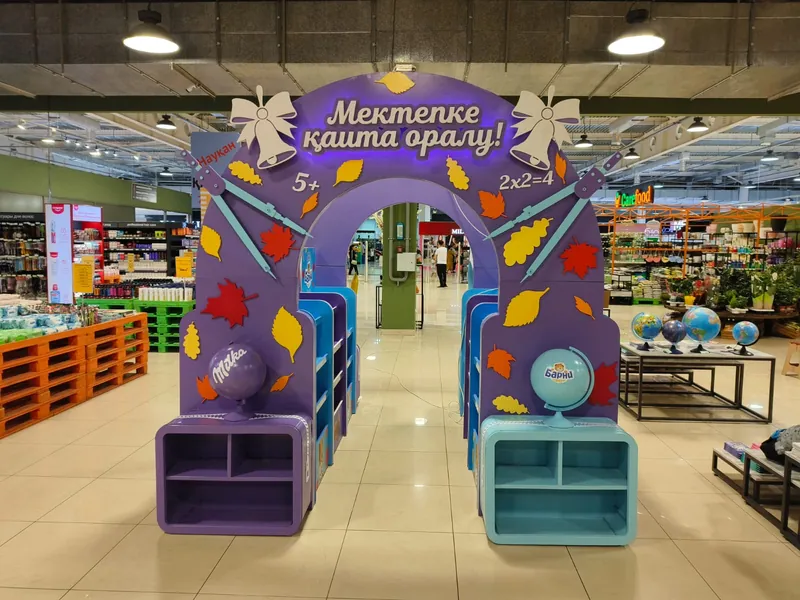 Зона бренда в торговом зале супермаркета: арка «Мектепке қайта оралу!» и фиолетовые и бирюзовые стеллажи