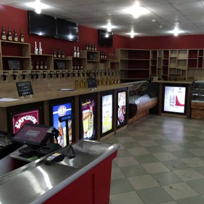 Стойка для разливных напитков: Стойка пивного магазина: ряд кранов, подсвеченные панели с пивными брендами, холодильная витрина, стеллажи