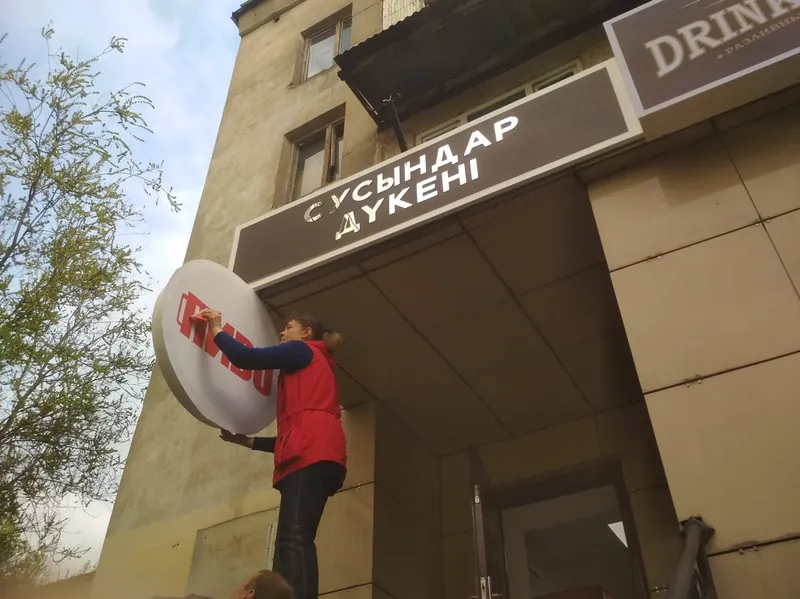 Монтаж вывески на фасаде магазина: круглый короб «ПИВО» под козырьком, рядом надпись «Сусындар дүкені»